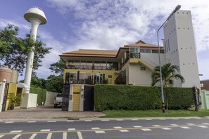 Un hôtel moderne doté d’un imposant château d’eau, d’une entrée sécurisée par un portail et d’une haie bien entretenue.