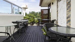 A rooftop patio with glass tables and wicker chairs, surrounded by potted plants and a view of the sky. - OYO 1005 Pacotte Boutique Resort (Rawai)