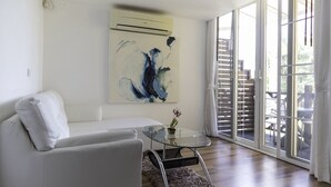 A modern living room with a white sofa, a glass coffee table, and a large abstract painting on the wall. - OYO 1005 Pacotte Boutique Resort (Rawai)