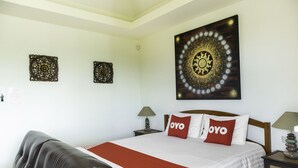 A neatly arranged hotel room with a large bed, two bedside tables, a brown leather sofa, and decorative wall art. - OYO 1005 Pacotte Boutique Resort (Rawai)