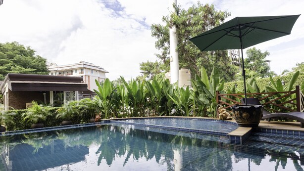 A swimming pool with a tiled edge, surrounded by lush greenery and a large umbrella. - OYO 1005 Pacotte Boutique Resort (Rawai)