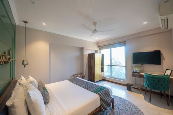 Una habitación de hotel moderna con una cama grande, un escritorio con silla, un televisor y una ventana con vistas.