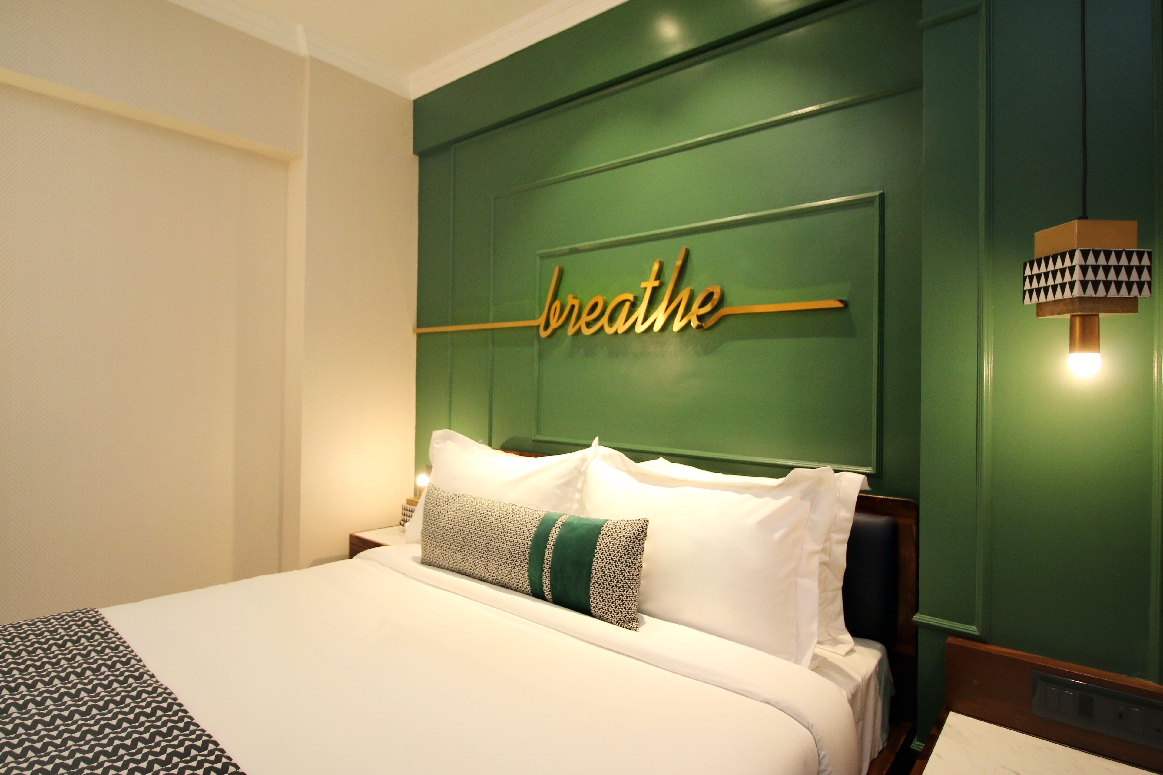 Une chambre d’hôtel avec un mur d’accent vert, un lit avec une literie blanche et un panneau indiquant « respirez » au-dessus de la tête de lit.