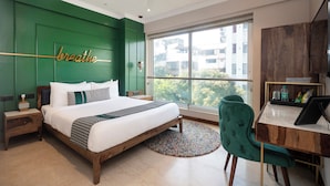 Une chambre moderne avec un grand lit, un bureau et une vue sur les immeubles par une grande fenêtre.