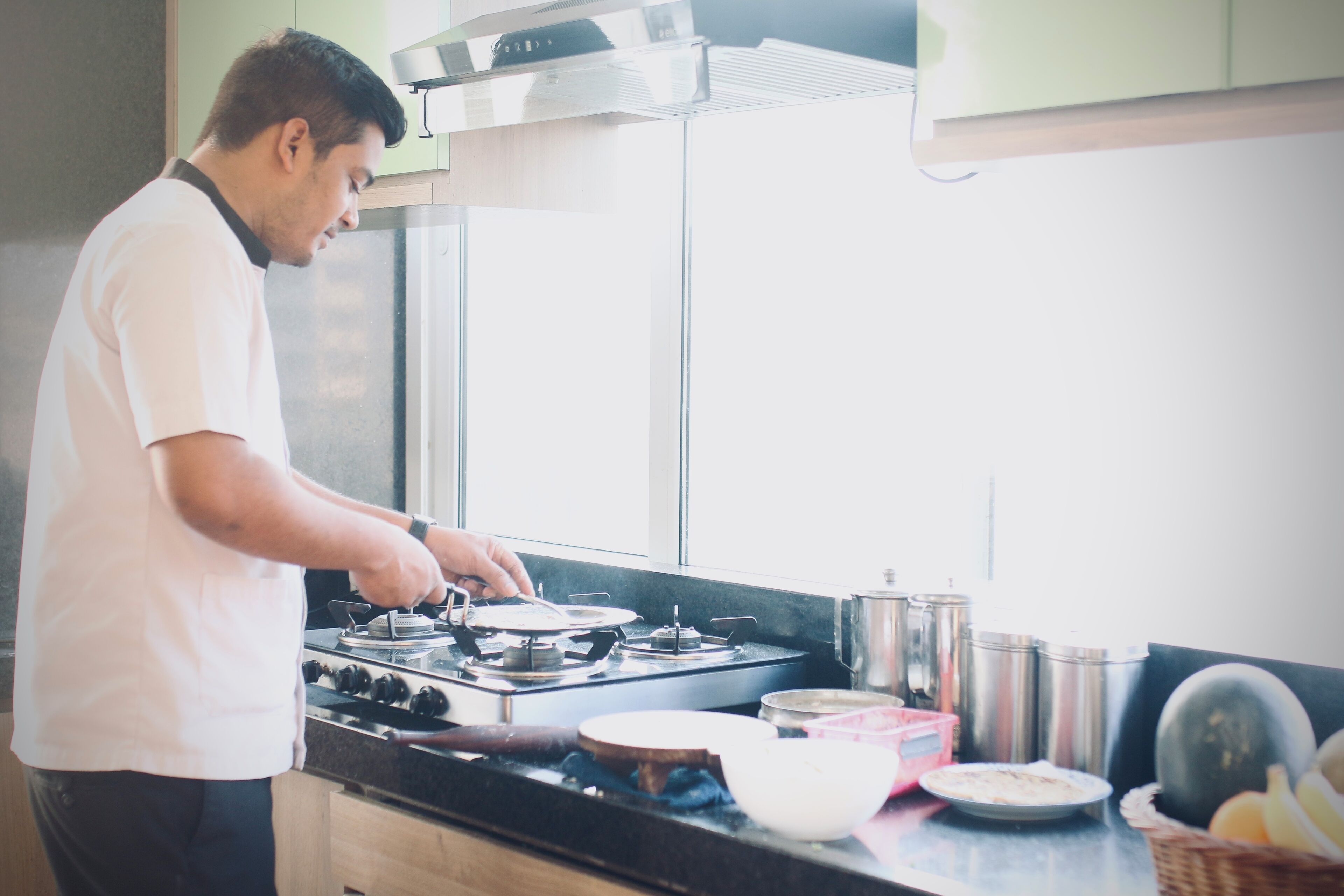 Una persona cocinando en una cocina con estufa, ollas y una ventana.