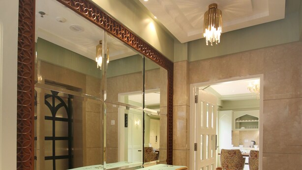 Une pièce spacieuse avec un grand miroir, une console décorative aux couleurs bleu et or, et un lustre.