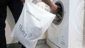 Een persoon houdt een witte waszak met tekst vast, staand naast een wasmachine.
