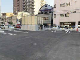 Um estacionamento com faixas demarcadas e um edifício com vários andares e varandas ao fundo.