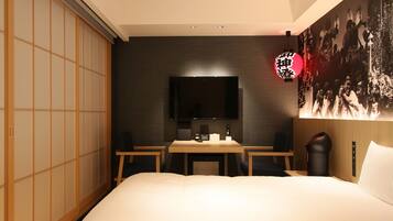 A hotel room with a bed, a dining table with chairs, a TV, and a sliding door.