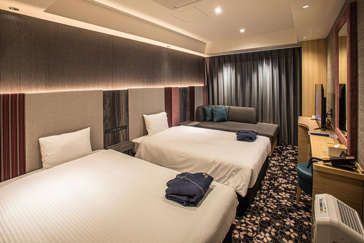 Une chambre d’hôtel avec deux lits, un bureau, une chaise, une télévision et un miroir.