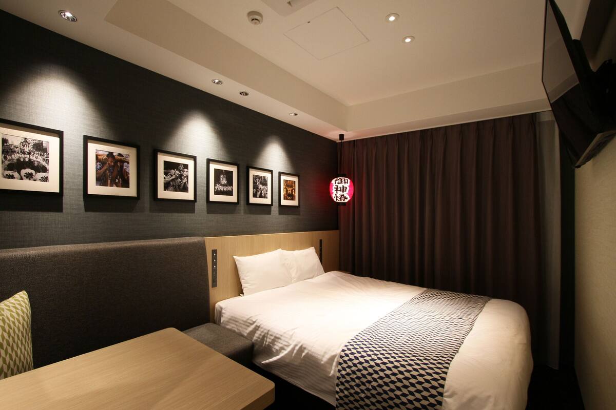 Une chambre d’hôtel comprenant un lit, une table de chevet en bois, un coin salon et un mur orné de tableaux.