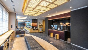 Un hall d’hôtel moderne doté d’un comptoir d’accueil, d’un espace salon et d’une grande fenêtre offrant une vue sur le paysage urbain.
