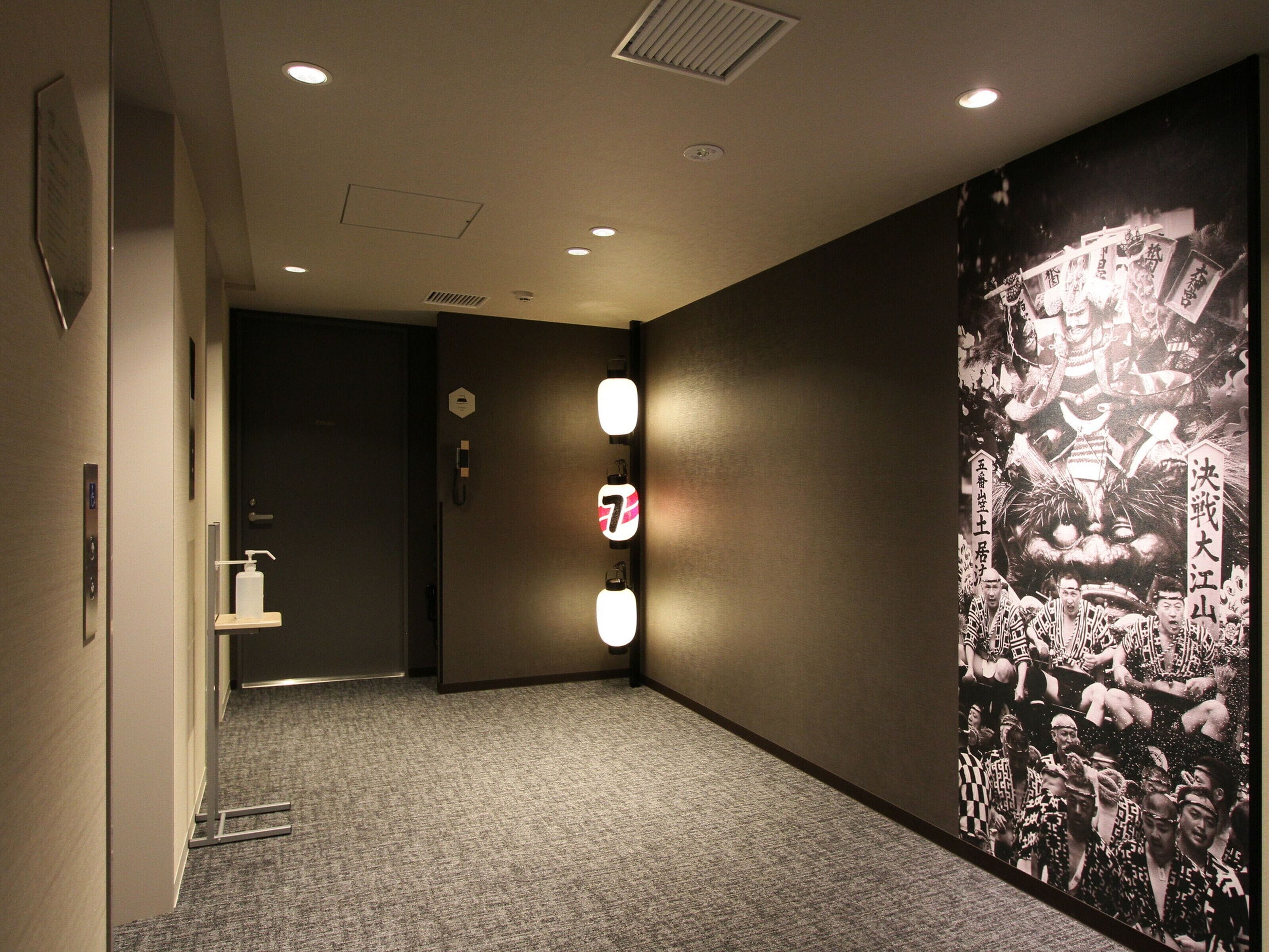 A hallway with a carpeted floor, a wall-mounted light fixture, and a large poster with indistinct text and images.