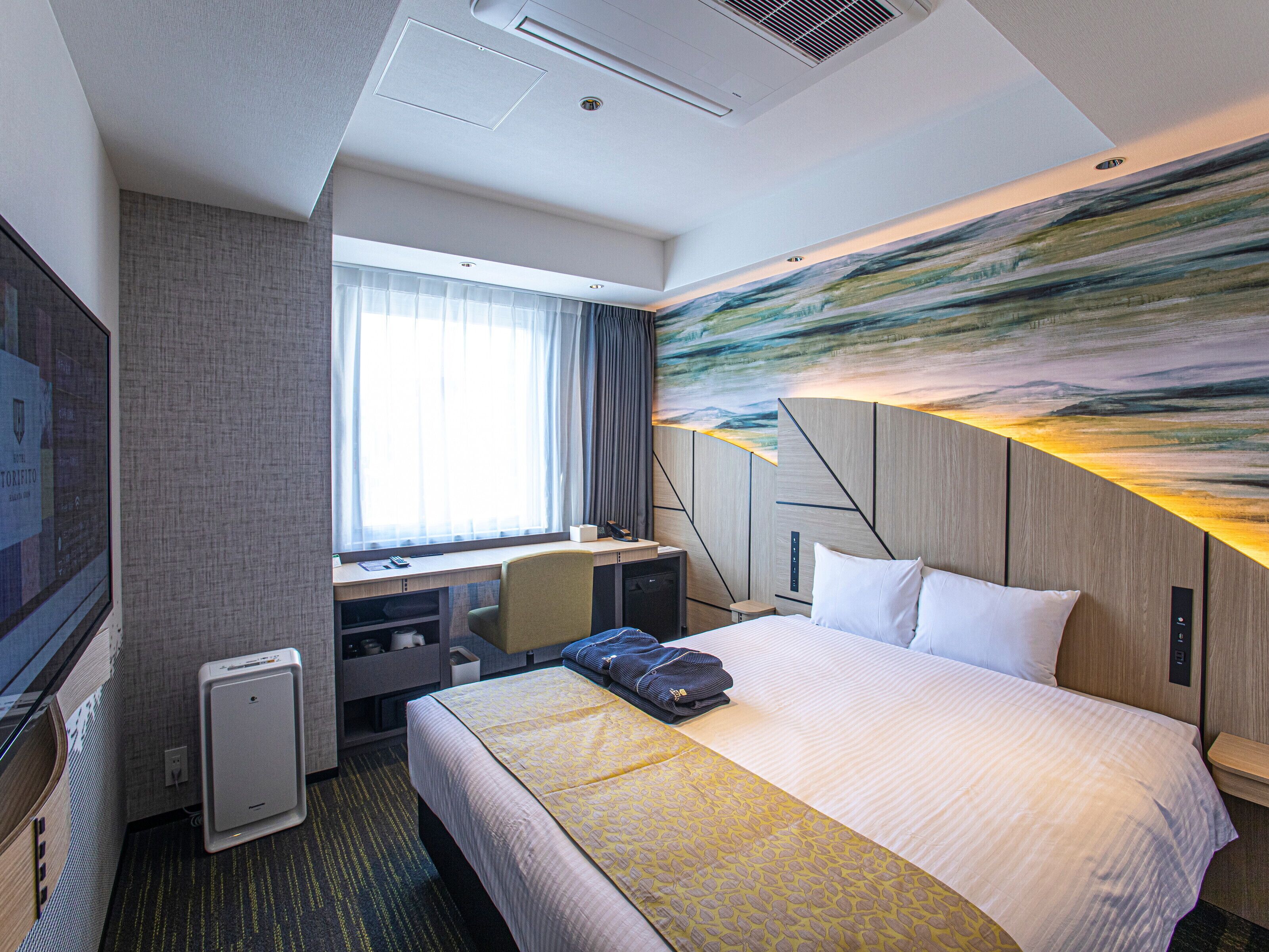 A hotel room with a large bed, a desk, a chair, and a TV.