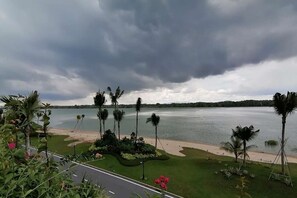 Blick auf einen Strand mit Palmen und Wasser unter einem bewölkten Himmel.