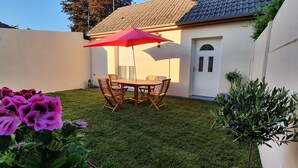 Eine Terrasse mit Tisch und Stühlen, einem roten Sonnenschirm und einer weißen Tür.