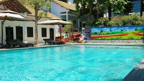 Une piscine avec des chaises longues et des parasols, une enseigne indiquant le «Song Khai Resort», et un bâtiment avec un toit en tuiles.
