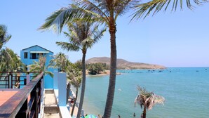 Un hôtel situé sur la côte, avec un bâtiment bleu, des palmiers et une vue sur la mer, où l’on peut apercevoir des bateaux.