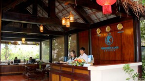 Un comptoir d’accueil avec un revêtement en bois, une grande fenêtre et un panneau indiquant que l’on se trouve au Songkhla Yai Resort.