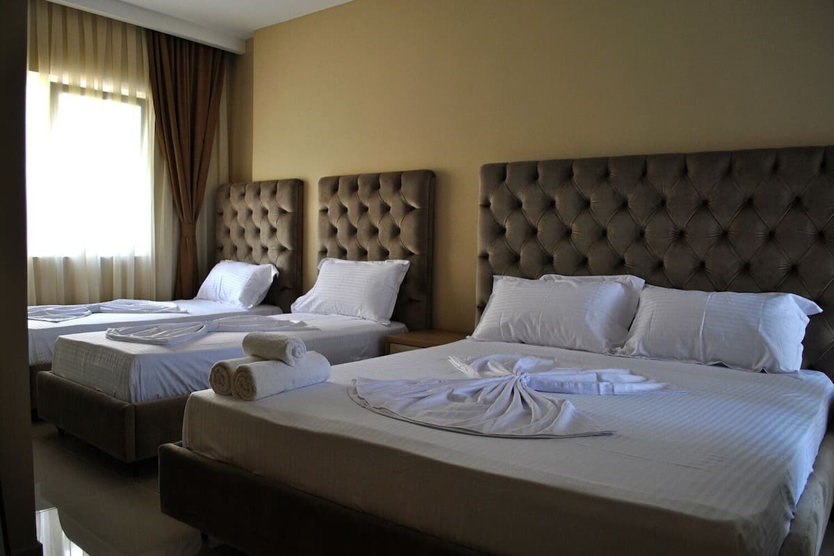 Ein Hotelzimmer mit zwei Betten, jeweils mit einem gepolsterten Kopfteil, weißen Leinentextilien und ordentlich drapierten Handtüchern.