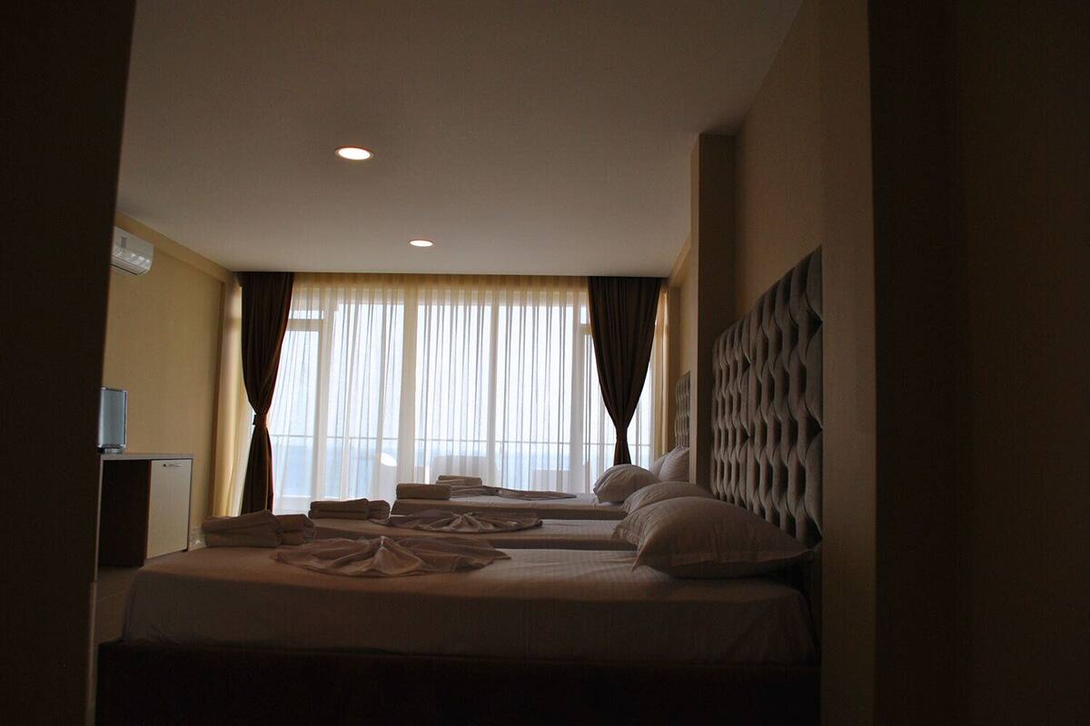 Ein Hotelzimmer mit zwei Betten, einem Flachbildfernseher und einem großen Fenster mit Vorhängen.