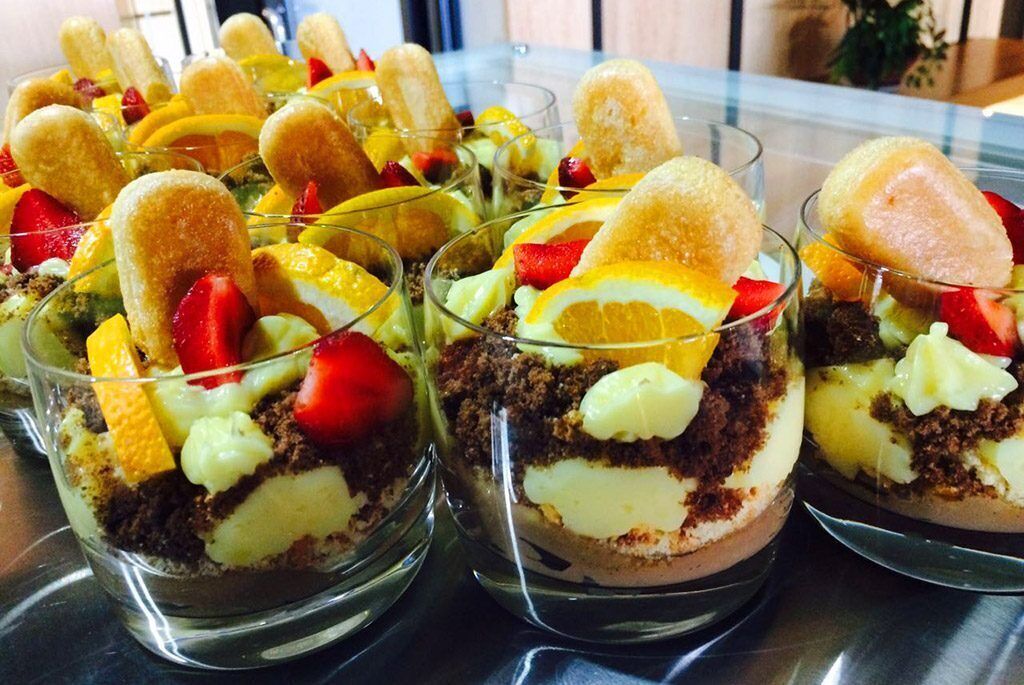 Vasitos de postre con capas de pastel, fruta y cobertura.
