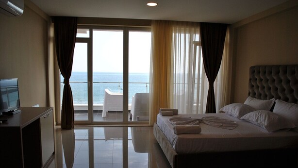Habitación de hotel con cama, escritorio con ordenador y vistas al mar a través de amplios ventanales.