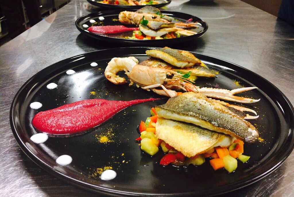 Ein Fischgericht mit Garnelen, Fisch und Gemüse auf einer schwarzen Platte.