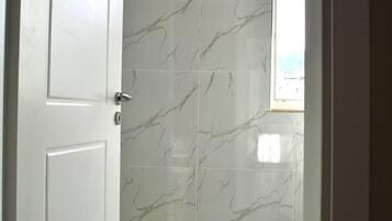 A bathroom with white marble tiles, a shower area, and a window.