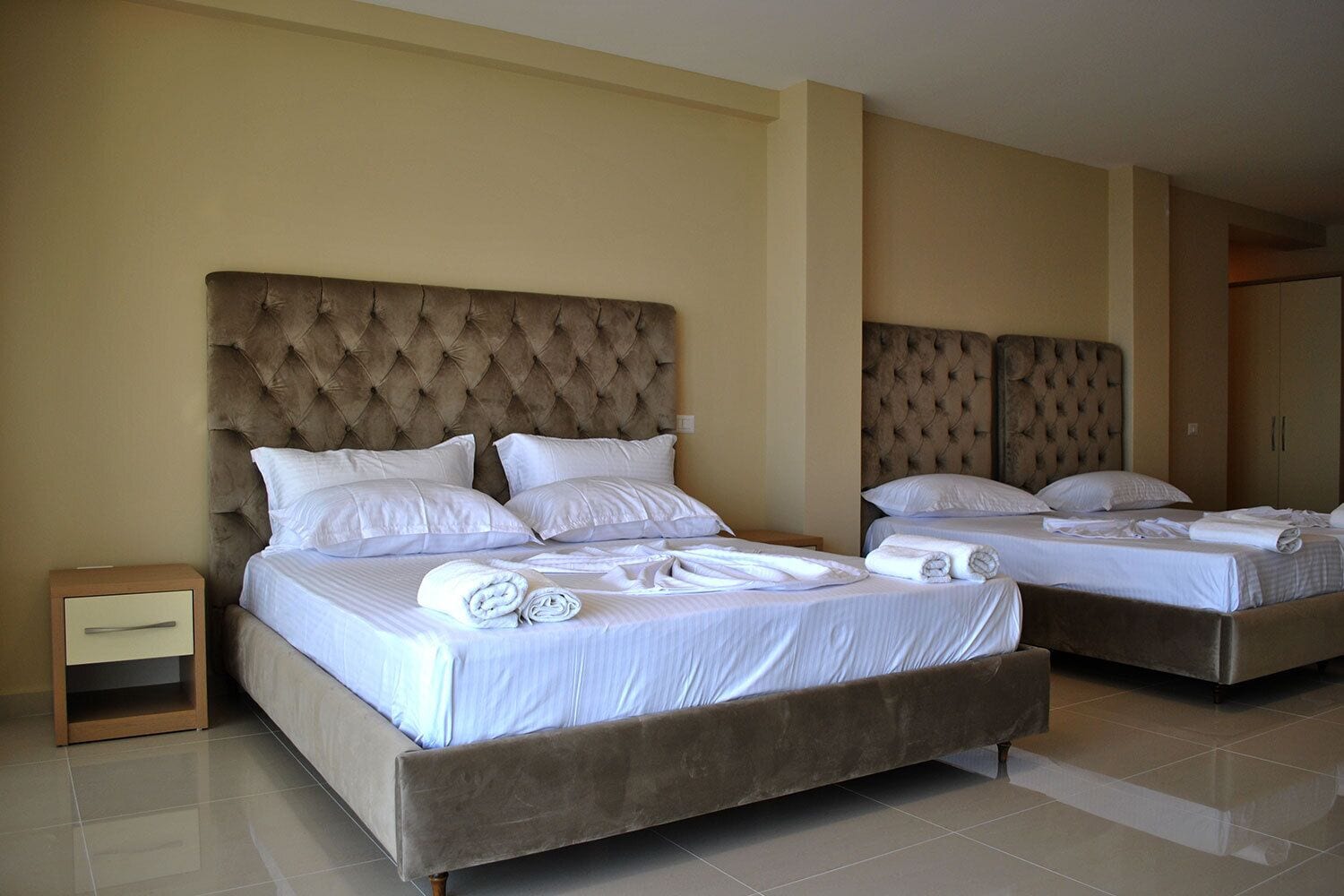 A hotel room with two beds, each with a tufted headboard, white bedding, and rolled towels on the beds.