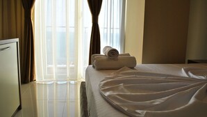 Una habitación de hotel con cama, una toalla enrollada y una ventana con cortinas.