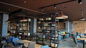 Un interior de restaurante moderno con techos altos, iluminación colgante y una pared de ladrillo. Mesas y sillas dispuestas para comer.