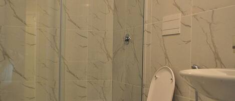 A bathroom with a glass-enclosed shower, a toilet, and a sink.