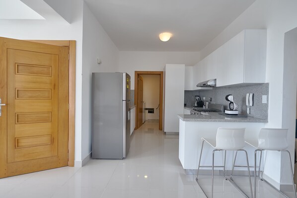 A modern kitchen with white cabinets, a built-in oven, and a countertop with bar stools. - Brand New Harmony Apartment w/Pool & Gym in La Julia (La Julia)