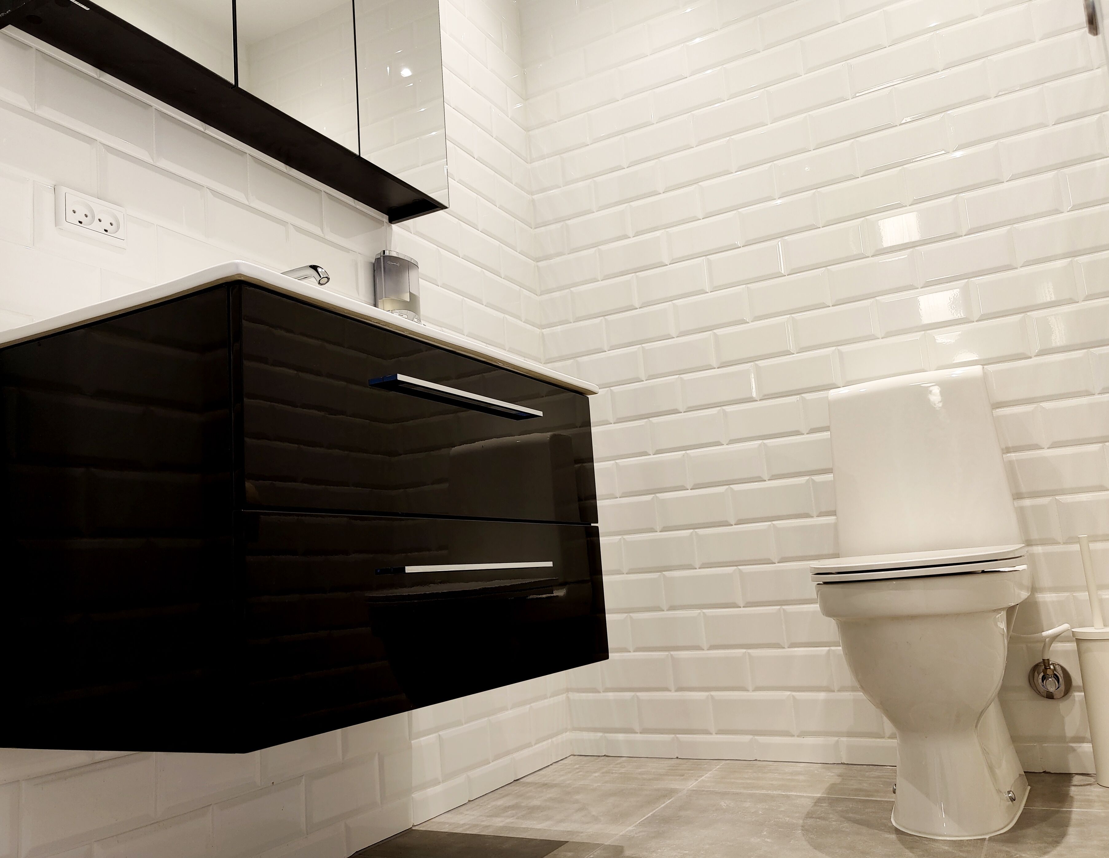 Ein modernes Badezimmer mit weißen Fliesen, einem schwarzen Waschtisch und einer weißen Toilette.
