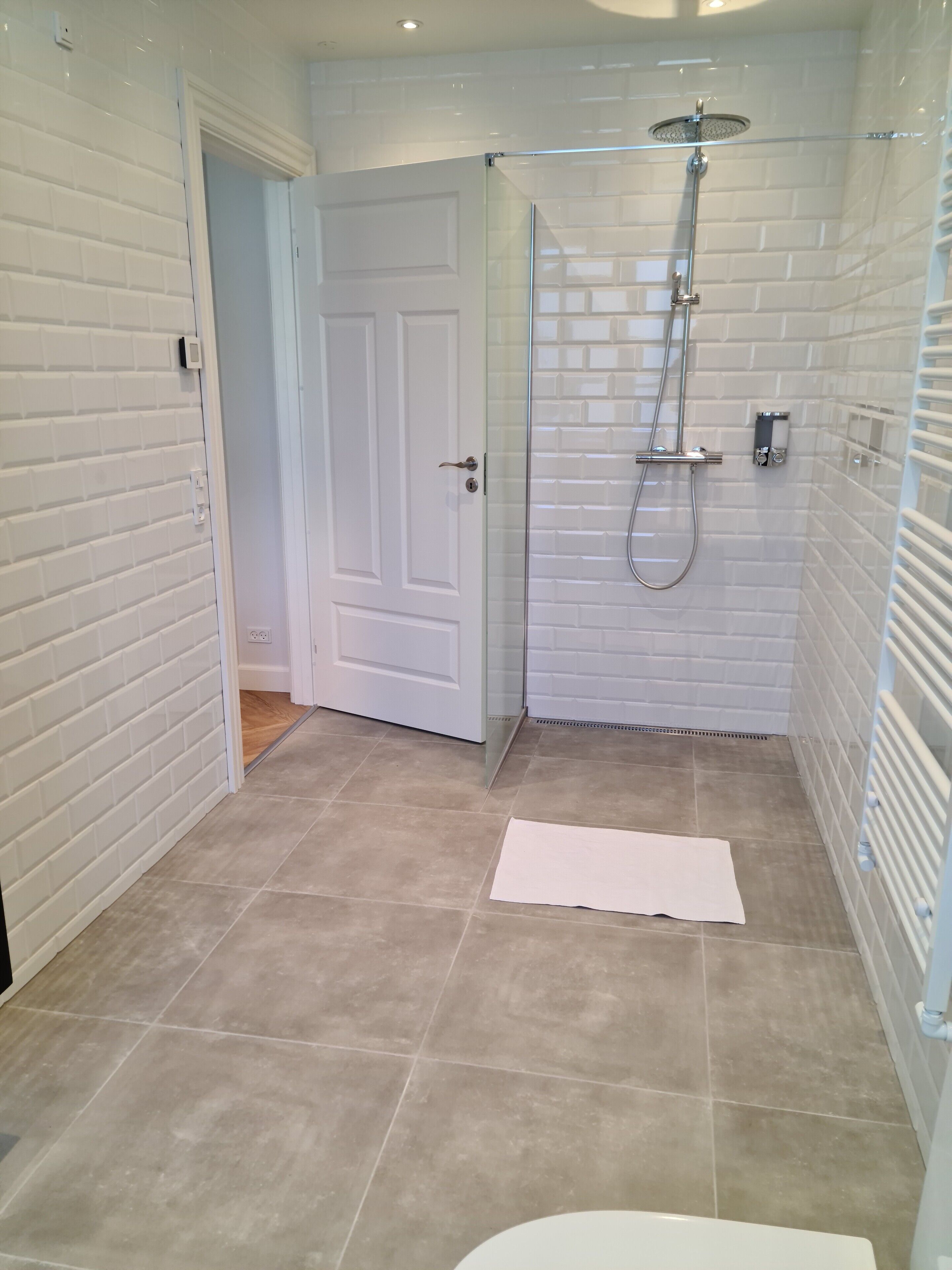 A modern bathroom with white tiled walls, a glass shower enclosure, and a white door.
