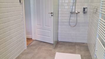 A modern bathroom with white tiled walls, a glass shower enclosure, and a white door.