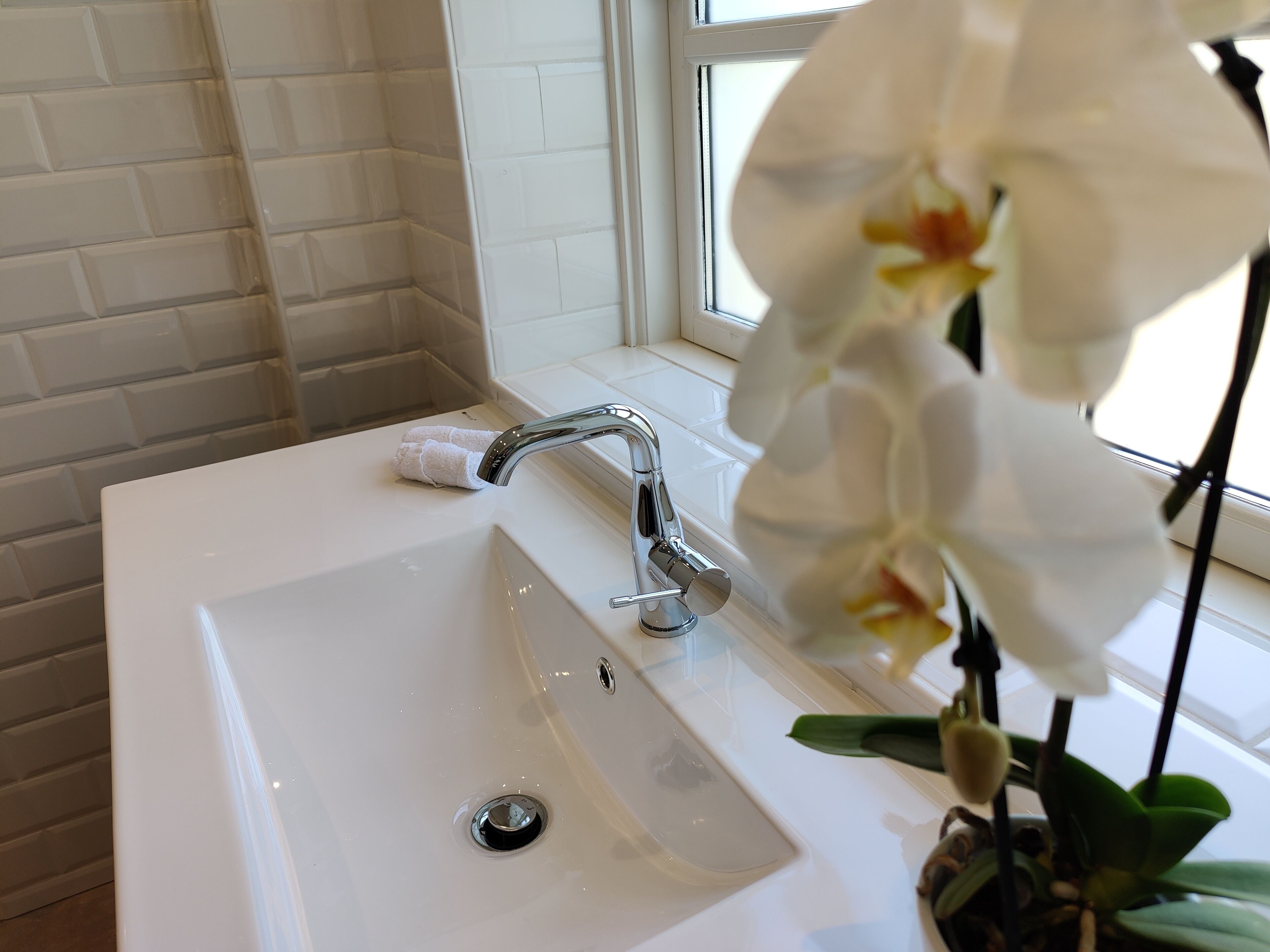 A bathroom with a white sink, chrome faucet, and a window with white curtains.