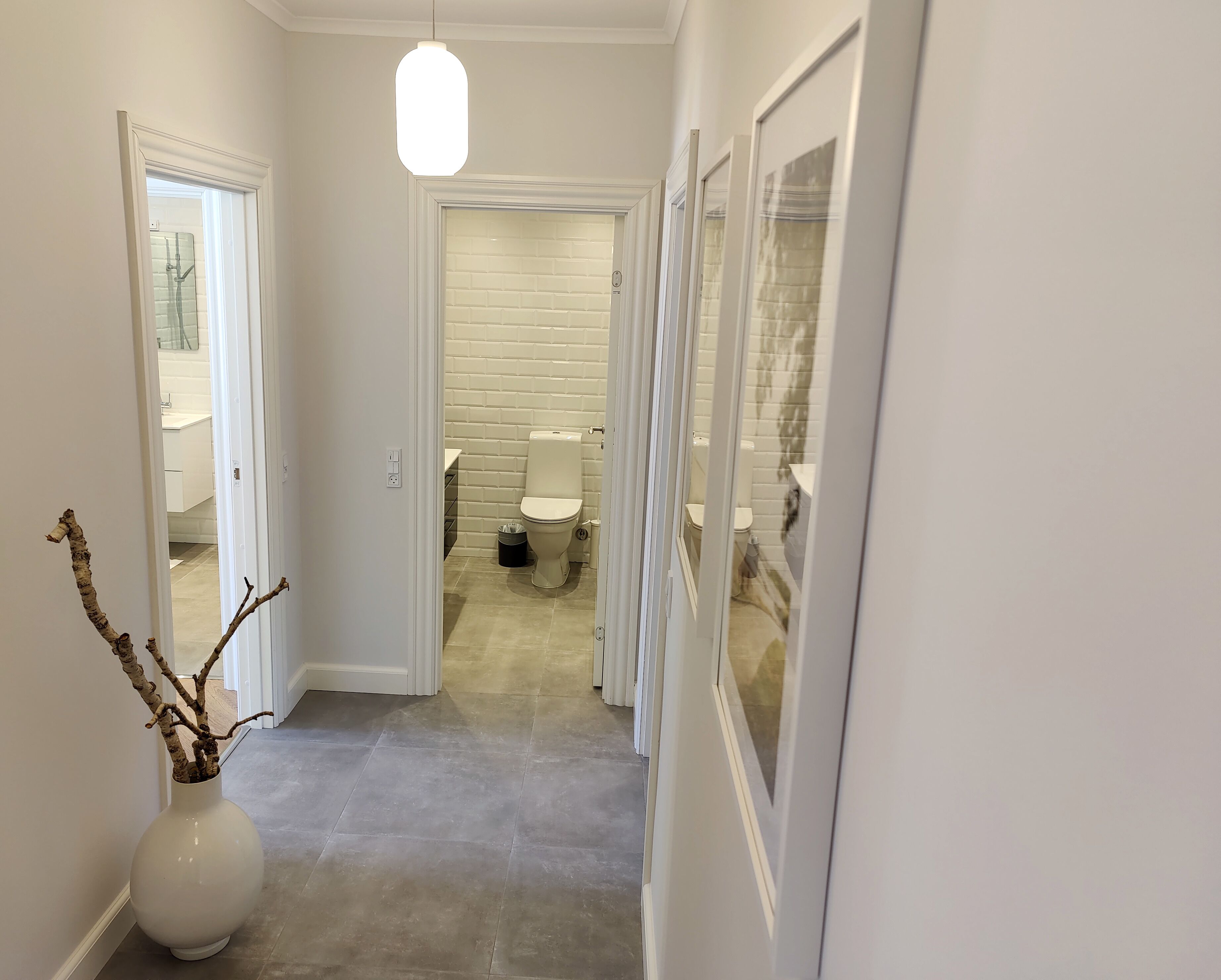 A hallway leading to a bathroom with a toilet, a trash bin, and a shower area.