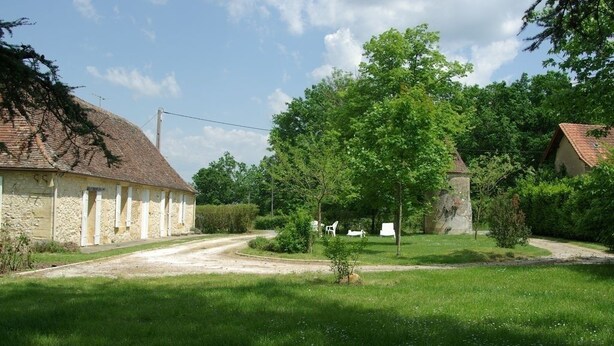 Een landelijk gelegen pand met een stenen gebouw, een onverharde weg en weelderige begroeiing.
