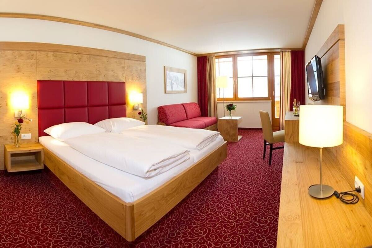 A hotel room with a large bed, a desk, a TV, and a window with curtains.
