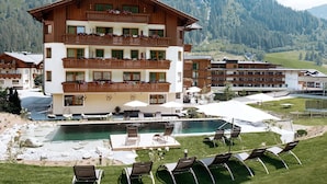 A multi-story hotel with a pool area, outdoor seating, and mountainous views. - Hotel Roslehen (Grossarl)