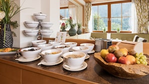 A breakfast buffet with various food items and bowls, a toaster, and a fruit bowl on a wooden counter. - Hotel Roslehen (Grossarl)