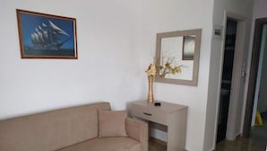 A room with a beige sofa, a small desk with a vase of dried flowers, a framed picture of a ship, and a mirror on the wall. - Central Hotel (Parga)