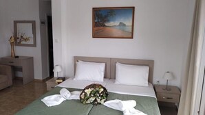 A hotel room with a bed, two bedside tables, a nightstand, a desk, a chair, and a painting of a beach scene. - Central Hotel (Parga)