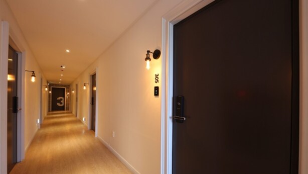 A hotel hallway with a wooden floor, a dark door on the right, and a number sign on the wall. - Cheonan Brown Dot Hotel Cheonan Station (Cheonan)