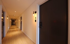 A hotel hallway with a wooden floor, a dark door on the right, and a number sign on the wall. - Cheonan Brown Dot Hotel Cheonan Station (Cheonan)