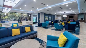 Un moderno vestíbulo de hotel con un amplio espacio de estar, una recepción y un mural de árboles.