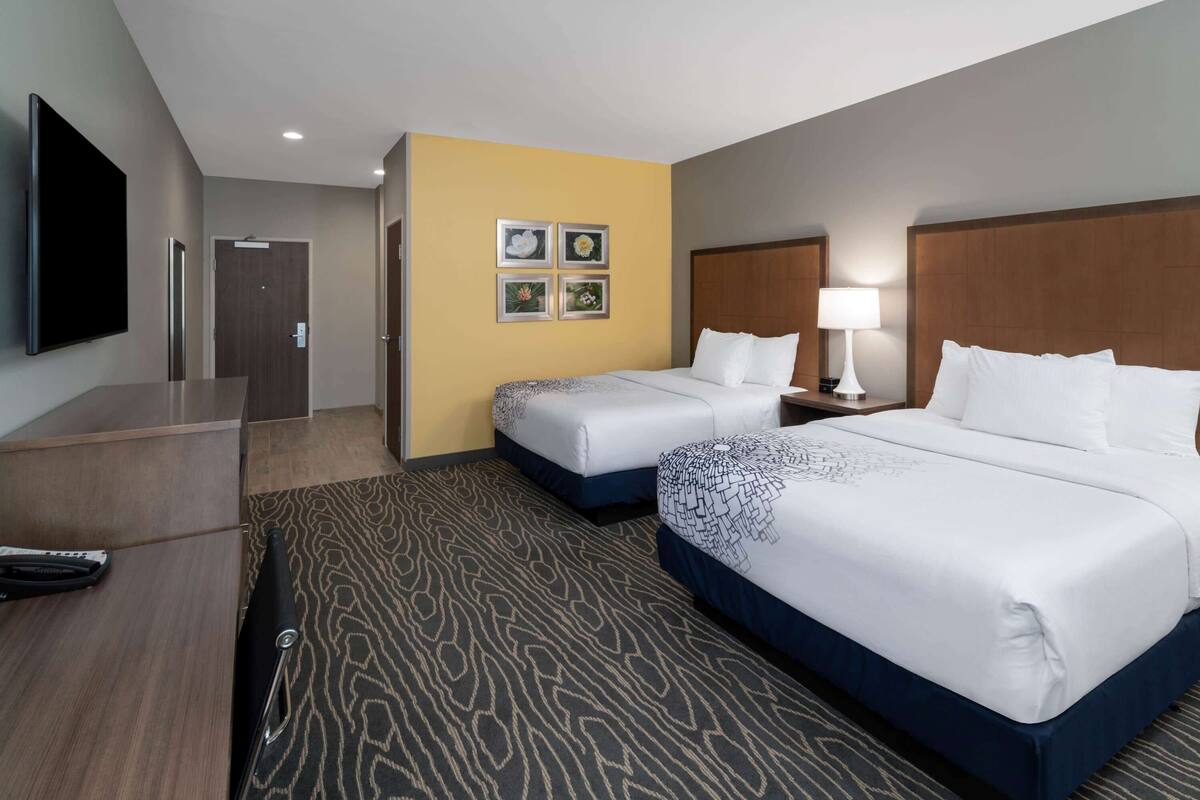 A hotel room with two beds, a desk, a TV, and a wall with four framed pictures.