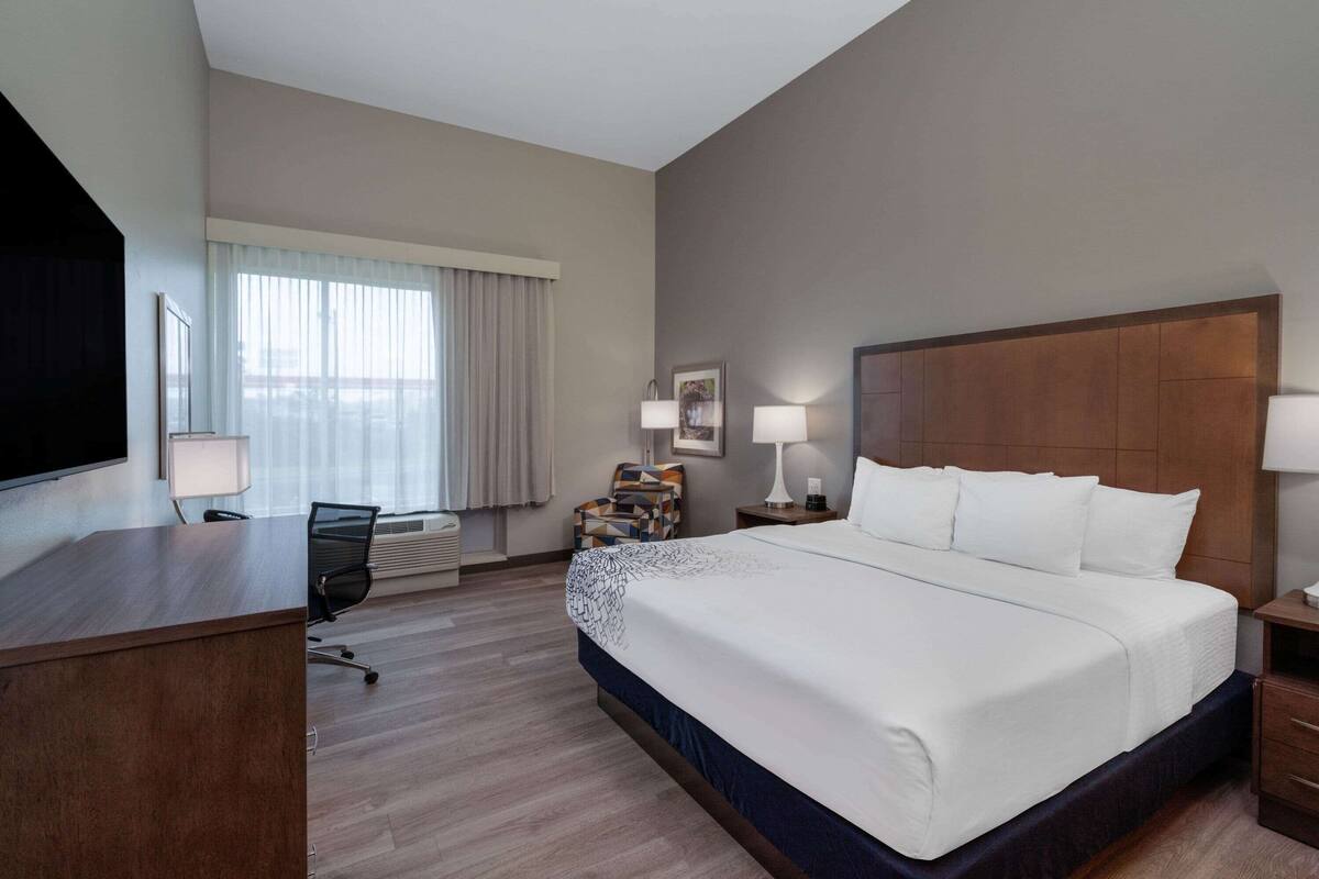A hotel room with a large bed, a desk, a chair, a TV, and a window with curtains.